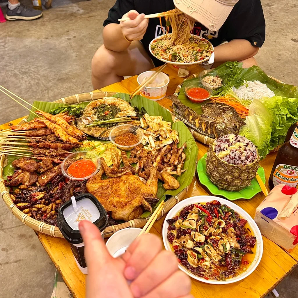 地道西雙版納傣味燒烤盛宴。烤魚、串燒、烤雞、菠蘿飯與香辣蘸料鋪在芭蕉葉上,是繽紛的雲南街頭美食。
