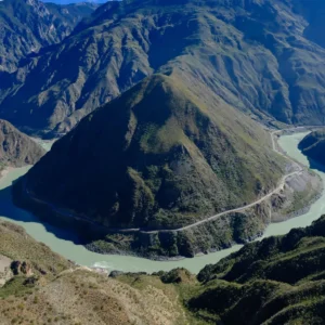 在 金沙江月亮湾 俯瞰，江水呈巨大弯曲环绕山体，宛如一轮弯月，公路沿山而行，景观壮丽震撼。
