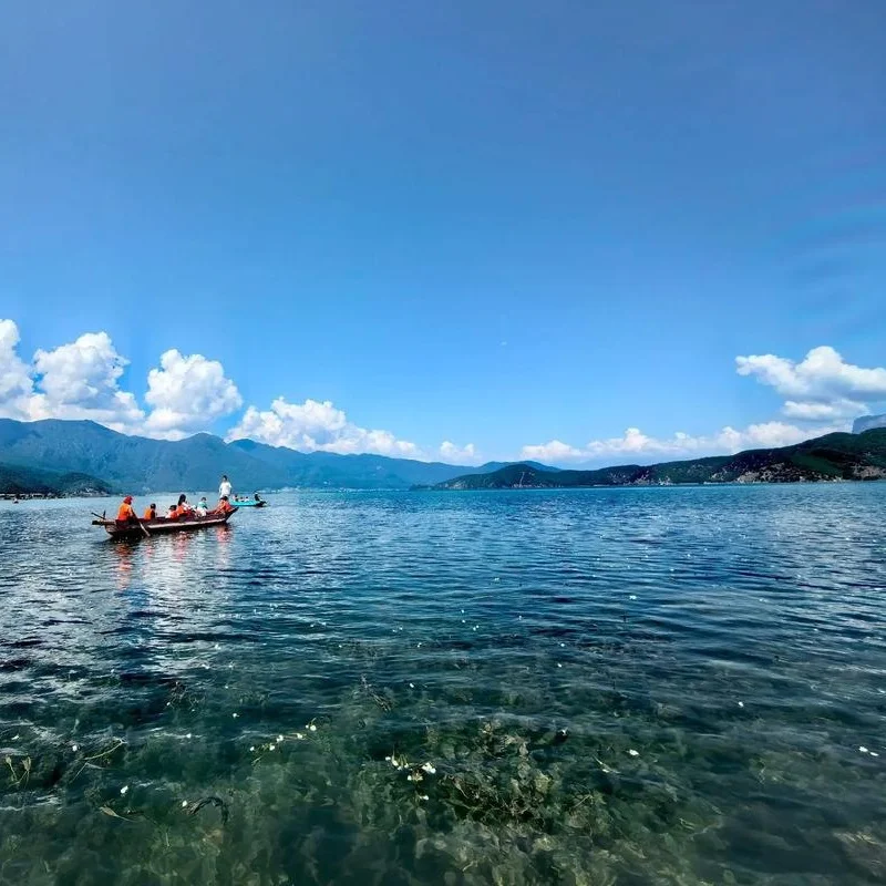 瀘沽湖的經典畫面:澄澈湖水、豬槽船與水面上的水性楊花,搭配藍天白雲與遠山,宛如人間仙境。