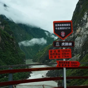 虎跳峽 G214 國道上的網紅打卡路牌，「世界的香格里拉，今生情定 G214」字樣格外醒目，背後是洶湧的金沙江與雲霧繚繞的峽谷。