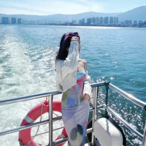 在 洱海 遊艇甲板上,一名女子迎著湖風站立,身後水花翻湧,遠方城市與群山相映。
