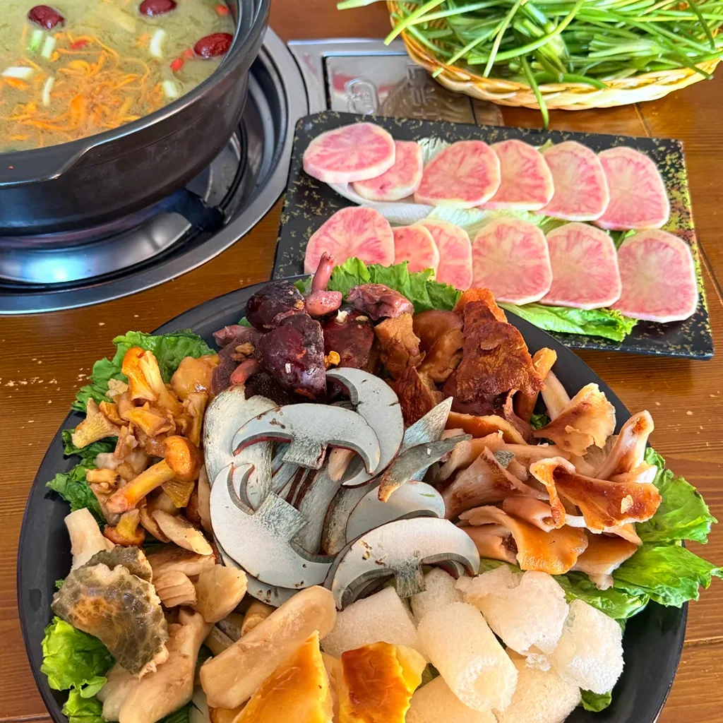 黑色大盤中擺放著多種新鮮野生菌切片,配上一鍋沸騰的高湯與粉紅色蘿蔔片,展現道地雲南風味。