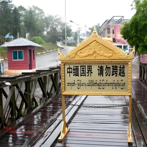 中緬邊境橋樑入口景象，橋面設有「中緬國界 請勿跨越」警示牌，周圍為邊境道路與哨所建築，展現中緬邊境地區的重要地理位置與跨國界線標誌