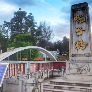 萬慶橋入口景觀，橋前立有刻著「萬慶橋」的石碑，旁邊是白色拱形橋體與紅色欄杆設計，周圍綠樹環繞與步道景觀，呈現邊境小鎮寧靜氛圍。此橋為當地具有歷史意義的地標之一，也是遊客參觀與拍照的熱門景點。