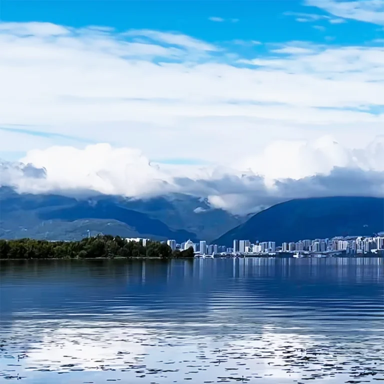 大理蒼山景觀,雲霧環繞山巒,前景為洱海水面,遠處可見城市天際線。