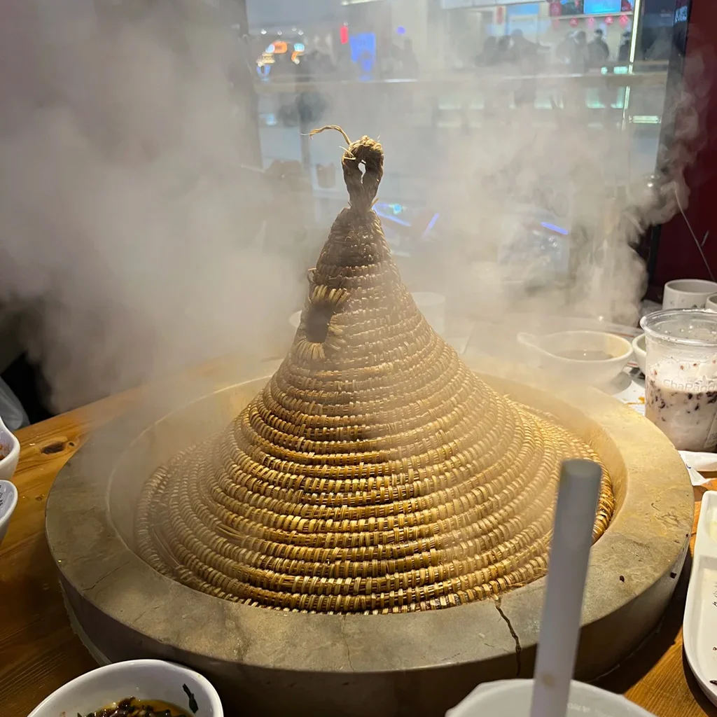 地道建水石鍋魚,雲南特色料理。新鮮魚類以手工雕刻石鍋蒸製,覆蓋編織圓錐草蓋,熱氣騰騰。
