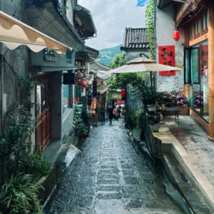 騰沖和順古鎮石板街巷景觀，兩側為傳統中式建築與特色店鋪，紅燈籠與庭院綠植點綴其間，遠處可見山景與遊客漫步其間，展現古鎮悠閒氛圍與濃厚歷史文化氣息。