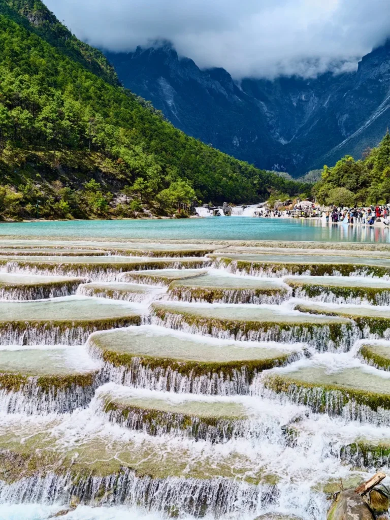 麗江藍月谷層層瀑布與藍色湖水,周圍環繞綠色山林。
