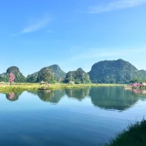 普者黑拍攝地壯麗的綠色喀斯特山丘倒映在平靜的藍色湖泊中,岸邊點綴著粉紅色的桃花樹。