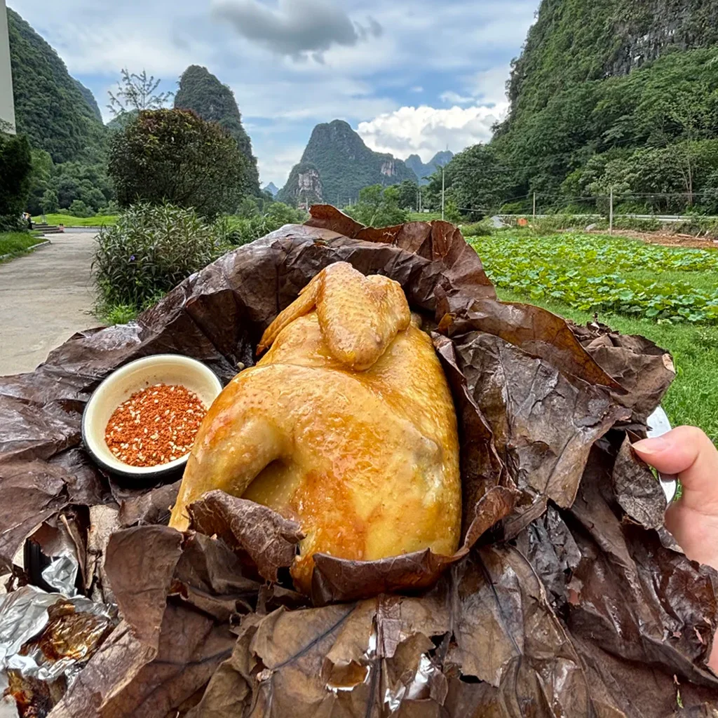 雲南文山普者黑的道地荷葉雞。多汁的整隻雞以香氣撲鼻的荷葉包裹,搭配辣椒蘸料,背景是喀斯特山景。
