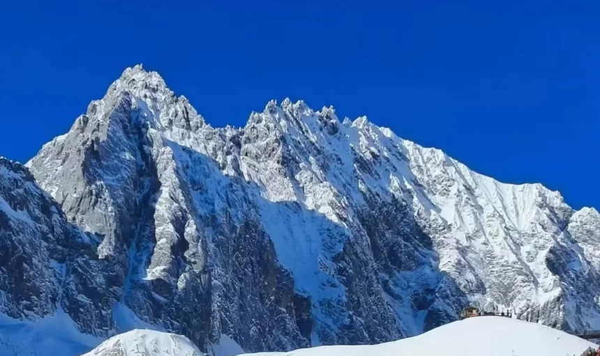 雲南麗江玉龍雪山,雄偉鋸齒狀積雪山峰聳立於澄澈深藍天空下,山腳有小型觀景平台。