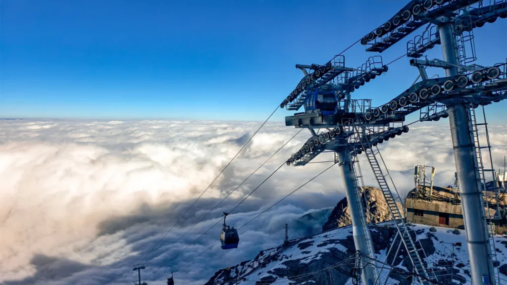 雲南麗江玉龍雪山冰川大索道,纜車飛馳於雲海之上,巨型鋼塔聳立,背景是積雪覆蓋的山巔。