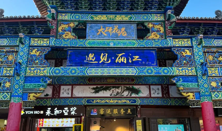 雲南麗江古城大研花巷,雕梁畫棟的傳統中式牌樓,「遇見・麗江」字樣,下方是在地店家,背景是澄澈藍天。