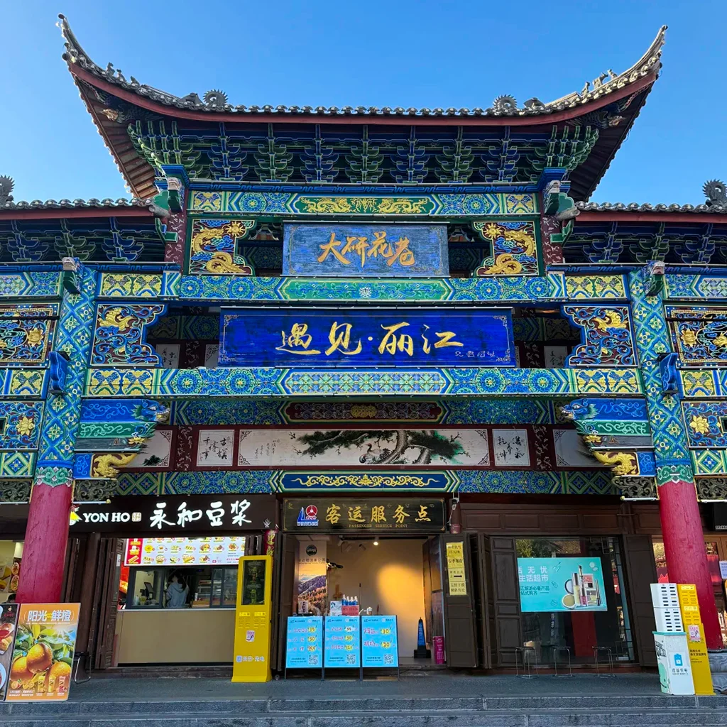 雲南麗江古城大研花巷,雕梁畫棟的傳統中式牌樓,「遇見・麗江」字樣,下方是在地店家,背景是澄澈藍天。