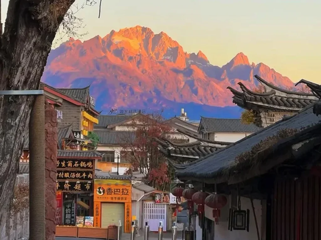 麗江古城眺望玉龍雪山的絕美「機位」,清晨日出時刻,雪山被金紅霞光染成「日照金山」奇景,前景是古色古香的納西建築。