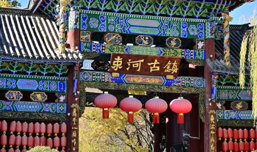 麗江束河古鎮大門牌樓，彩繪雕花古建飛檐，滿掛喜慶紅燈籠，在湛藍晴空下盡顯千年納西古韻。