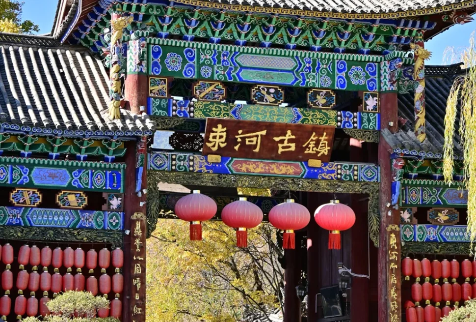 麗江束河古鎮大門牌樓，彩繪雕花古建飛檐，滿掛喜慶紅燈籠，在湛藍晴空下盡顯千年納西古韻。