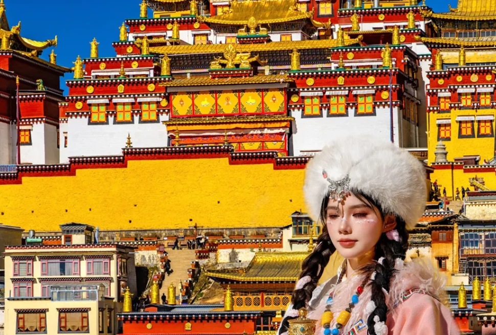 在 松贊林寺 前，遊客身著藏族傳統服飾拍照留念，金頂寺廟群莊嚴宏偉，色彩鮮豔，人物與藏式建築相互映襯，充滿民族風情。