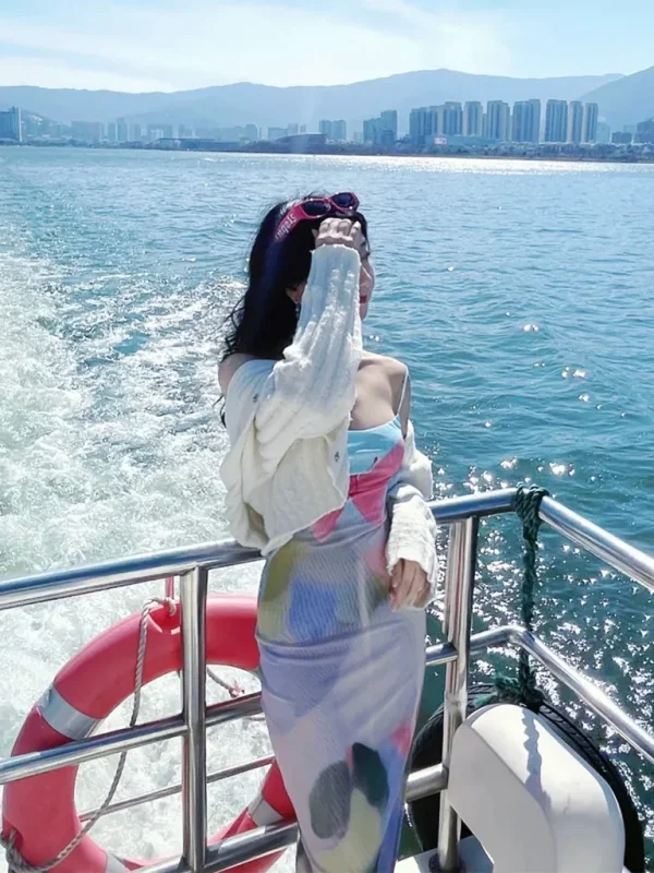 在 洱海 遊艇甲板上,一名女子迎著湖風站立,身後水花翻湧,遠方城市與群山相映。