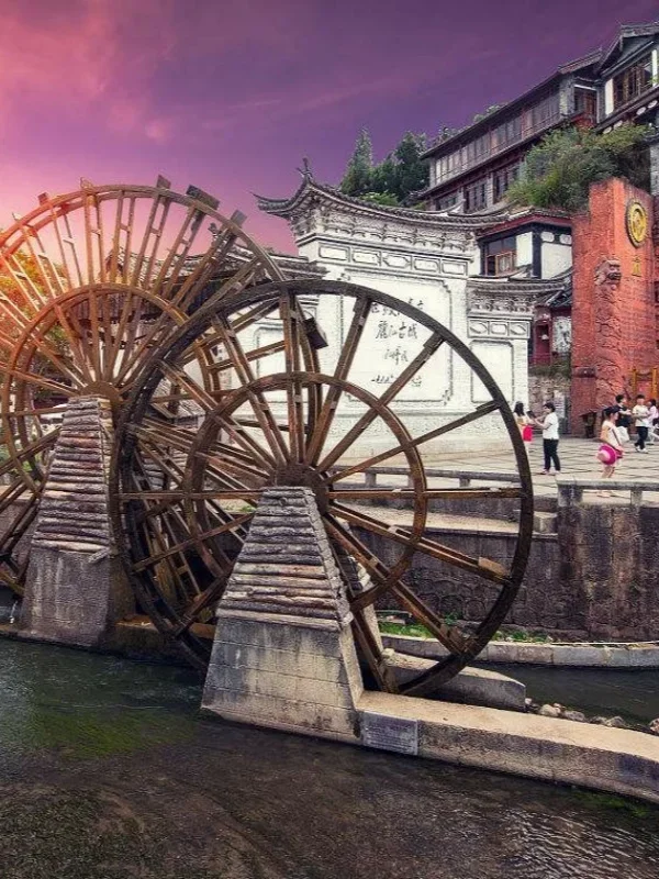 麗江古城著名的大水車景觀,巨大的木製水車在清澈河道旁緩緩轉動,周圍是傳統納西族建築與古城街景。